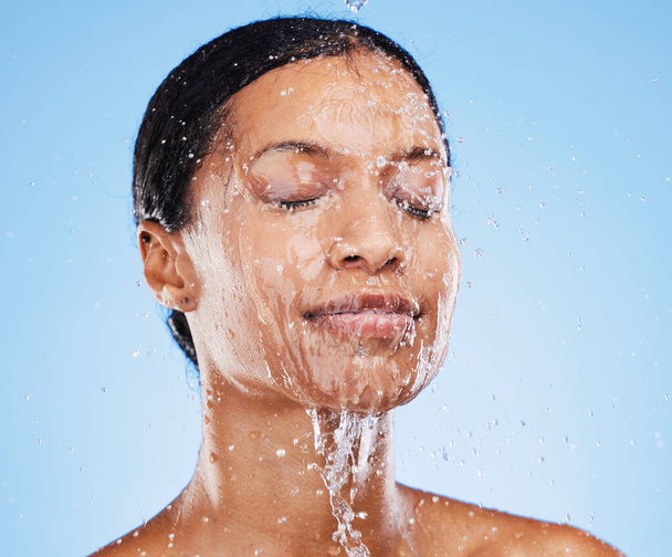 Woman, shower and water splash on face for skincare hydration or clean hygiene against blue studio background. Female in facial wash with water to hydrate or cleanse for hygienic body care treatment. - Photo, Image