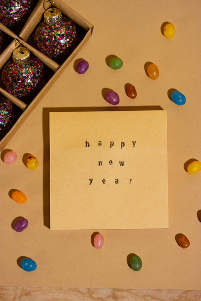Happy New Year 2023 text printed on an old retro typewriter on a notebook, colorful candies scattered on a table. Christmas winter holidays, vacations fun. Vertical brown cell phone vintage wallpaper. - Φωτογραφία, εικόνα
