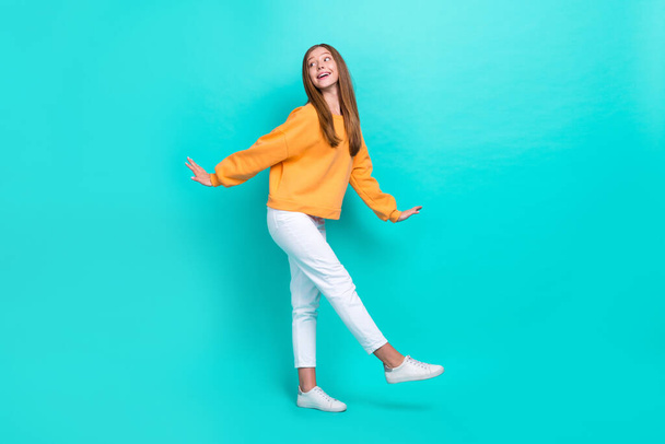 Full length size photo of excited child girl dancing wear orange sweater white pants look empty space dreamy isolated on aquamarine color background. - Фото, изображение