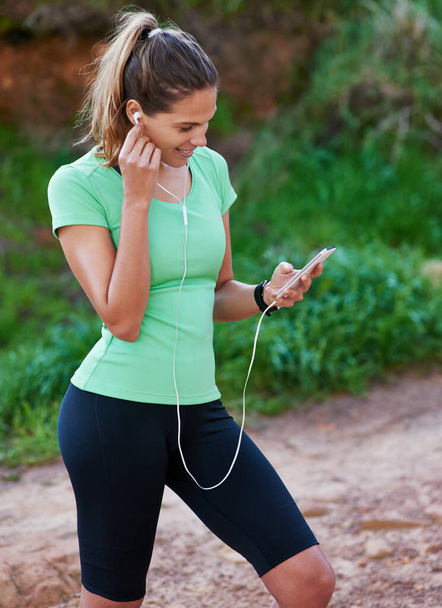 Choosing some tunes for the trail. a young woman listening to music while exercising in the outdoors - Foto, Imagen