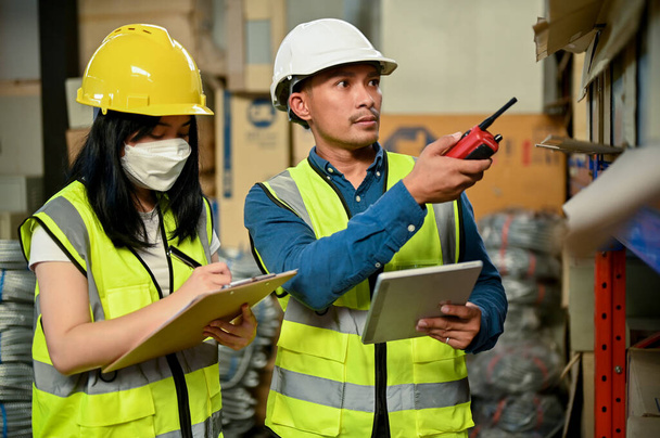 Professional adult Asian male warehouse supervisor training a new female worker, checking their inventory in the warehouse or storehouse. - Photo, image