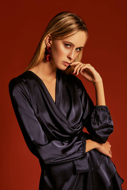 Seductive close up photo of beautiful blonde girl in cocktail silk dress, seduces someone touching her lips by her finger - Фото, зображення
