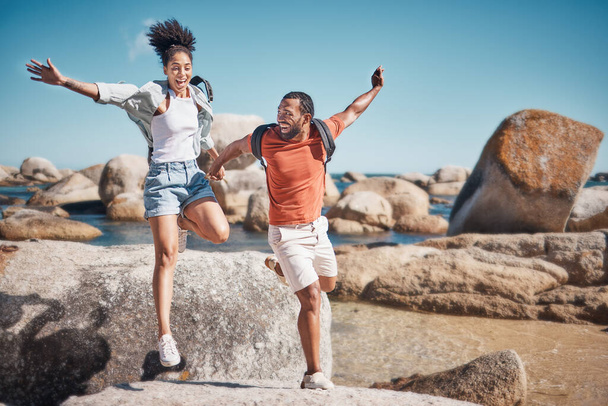 Beach, freedom and happy couple jumping on rocks together while on seaside summer vacation. Happiness, travel and young man and woman in nature by the ocean on holiday, adventure or journey in Mexico. - Fotografie, Obrázek