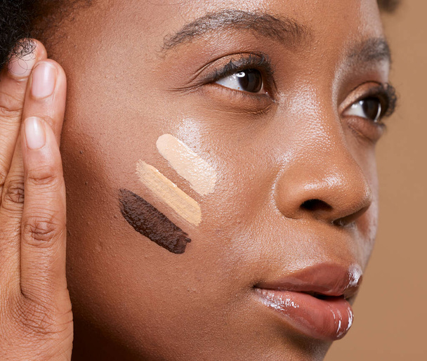 Ομορφιά, μακιγιάζ και foundation αποχρώσεις στο πρόσωπο της μαύρης γυναίκας με Swatch για καλλυντικά, ποικιλία ή βασικό τόνο. Όψη, προϊόν και αίγλη με διαφορετικό χρώμα στο γυναικείο μοντέλο για κονσίλερ ή υφές. - Φωτογραφία, εικόνα