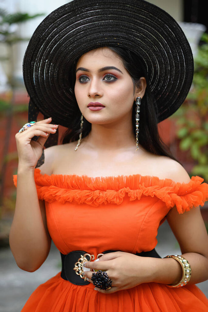 Porträt einer jungen schönen modernen Inderin in westlichem Outfit mit schwarzem Strohhut, die modisch vor verschwommenem Hintergrund posiert. Lifestyle und Mode. - Foto, Bild