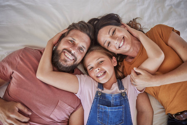 Family, portrait and relax in bed by girl and parents resting from above, happy and smile in home together. Happy family, love and face of child with mom and dad in bedroom for bond and hug. - Photo, Image