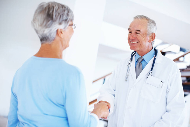 Mature doctor and woman shaking hands. Smiling mature doctor shaking hands with woman in hospital - Photo, image