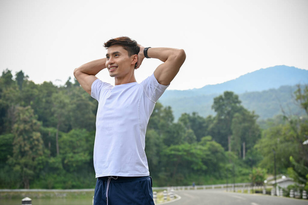 Yakışıklı ve sportif formalı genç Asyalı adam ellerini başının arkasına koyup derin bir nefes alıyor, uzun bir koşudan sonra dinleniyor.. - Fotoğraf, Görsel