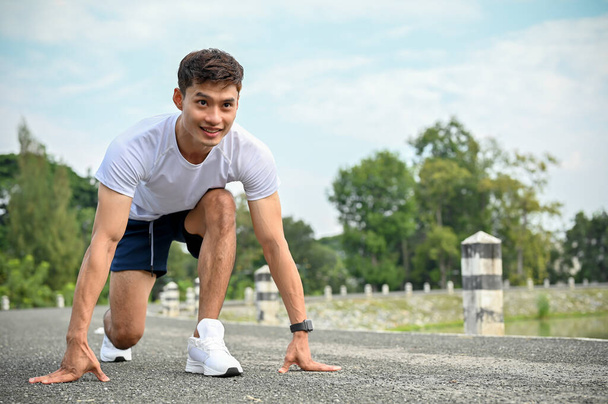 Guapo determinado atlético joven asiático en ropa deportiva preparándose para correr, posición de partida estable. Entrenamiento, entrenamiento, ejercicio - Foto, Imagen
