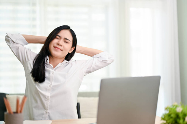 Attraente giovane donna d'affari asiatica o donna manager mani dietro la testa, gli occhi chiusi, rilassante alla scrivania in ufficio. - Foto, immagini