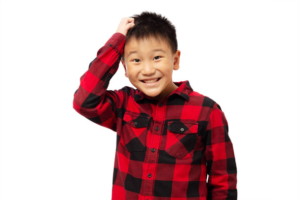 Αστείο παιδί ξύνει το κεφάλι φορώντας κόκκινο πουκάμισο απομονωμένο σε λευκό φόντο - Φωτογραφία, εικόνα