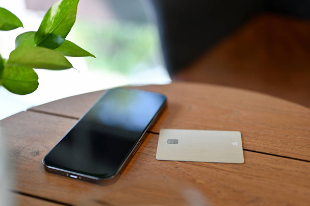 Kreditní karta a smartphone jsou na dřevěném stole. bezhotovostní platba, mobilní bankovnictví, převod peněz, nakupování přes internet. oříznutý obrázek - Fotografie, Obrázek