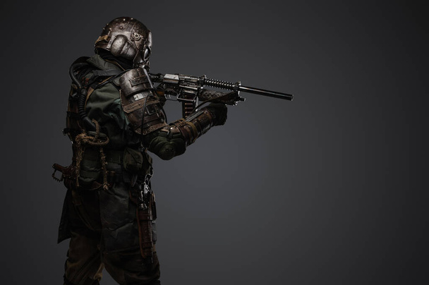 Portrait of military man in post apocalypse style dressed in armored suit aiming shotgun. - Фото, изображение