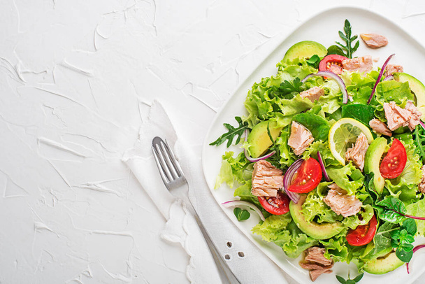 Fresh green leafy salad with tuna avocado and tomato on white table background. Concept for a tasty and healthy meal - Foto, imagen