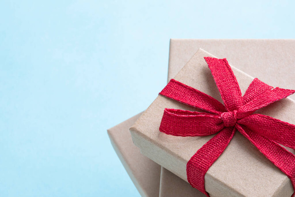 Closeup brown paper gift box with red textured ribbon bowtie on the pile of other gift boxes with light blue background and copy space - Photo, Image