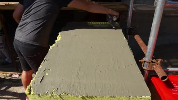 Vista sobre la mano del trabajador con paleta, aplicando pegamento sobre lana mineral amarilla para aislar el edificio, obra.  - Metraje, vídeo