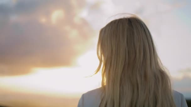 Atrakcyjna kobieta ciesząca się zachodem słońca zbliżenie nieba. Blondynka patrząca na portret przez ramię. Delikatna twarz dziewczyny oglądającej letni krajobraz samotnie. Kobieta model stwarzający zachmurzone tło natury - Materiał filmowy, wideo