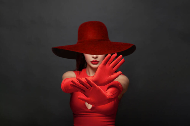 Ferma il gesto. Bruna donna mani in guanti di seta rossi e largo cappello tesa mostrando gesto di stop, negazione, negazione e no. Stop concetto di violenza - Foto, immagini