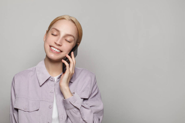 Akıllı telefon tutan ve beyaz stüdyo duvarında iletişimin keyfini çıkaran mutlu güzel bir kadın. - Fotoğraf, Görsel