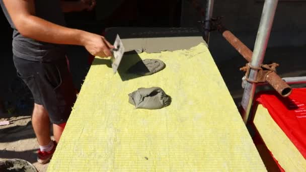 Vista sobre la mano del trabajador con paleta, aplicando pegamento sobre lana mineral amarilla para aislar el edificio, obra.  - Metraje, vídeo