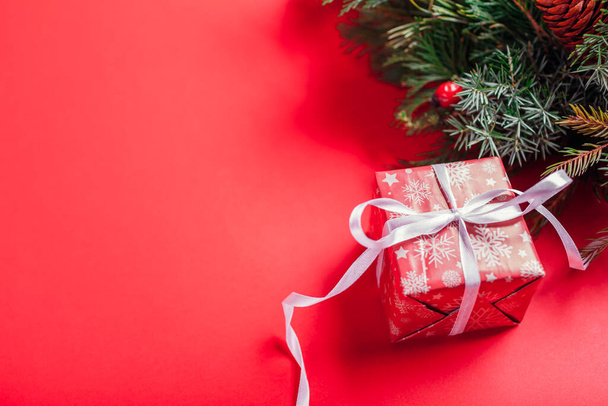 Vánoční a novoroční dárková krabice zabalená do slavnostního červeného papíru a stuhy po jedlovém věnci. Dárek na zimní dovolenou na červeném pozadí. Space mock-up - Fotografie, Obrázek
