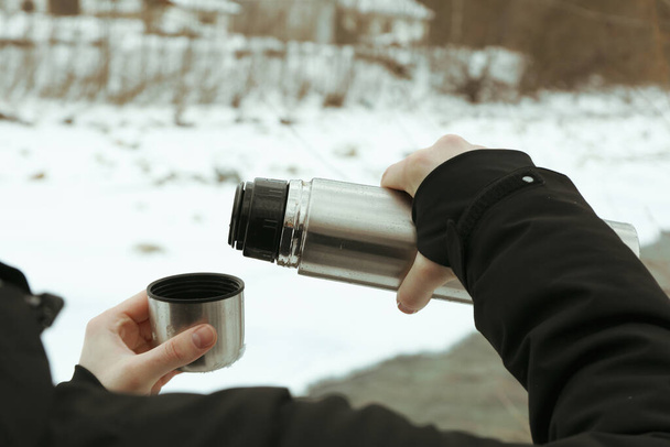 A man pours a drink from a thermos into the lid outdoor - Foto, Imagen