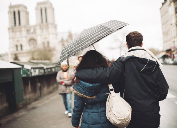 een verliefd stel dat samen onder een paraplu in Parijs loopt tegen de achtergrond van de Notre Dame kathedraal - Foto, afbeelding