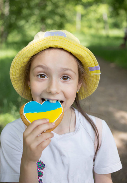 Ukrayna bayrağının sarı-mavi renklerine boyanmış zencefilli çöreğiyle 7 yaşındaki sevimli bir kızın yüz portresi. Ukraynalı olmaktan gurur duyuyorum. Ukrayna 'ya bayılırım. Savaşı durdurun. Ukrayna 'yı Destekle - Fotoğraf, Görsel