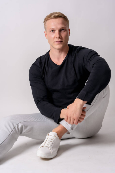 Caucasian blonde model in a black sweater on a white background, staring at the camera - Foto, Bild