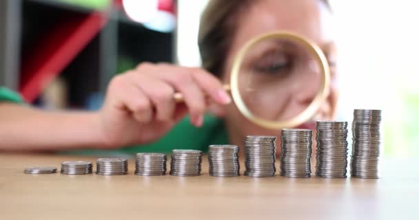 Emotions of excited greedy business woman looking at growing stack of coins through magnifying glass. Growth in financial cash income - Footage, Video