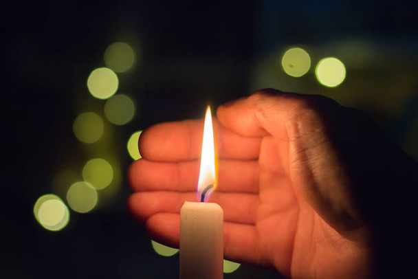The hand closes the fire of a candle in a dark room. Blackout in Ukraine due to war - Fotó, kép