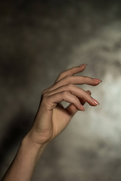 Close-up of a beautiful female hand with a simple nail manicure, on a gray background, selective focus. Weave long fingers and a fragile wrist, plastic movement. - Zdjęcie, obraz