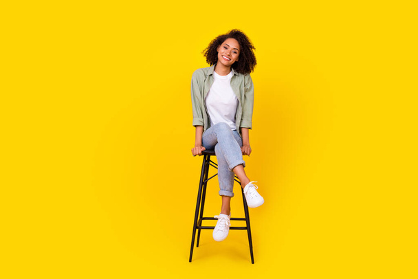 Full size photo of cheery young woman curly hair sit chair have rest chatting wear trendy khaki outfit isolated on yellow color background. - Photo, Image
