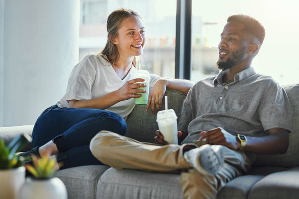 Love, healthy and smoothie with a diversity couple on a sofa in the living room of their home to relax together. Weight loss, diet and nutrition with a man and woman drinking a shake for detox. - Foto, Imagem