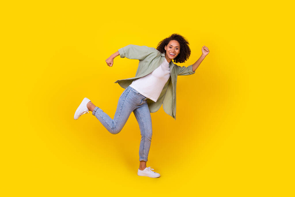 Full body foto van grappige jonge vrouw krullend haar lopen snelle hobby vrije tijd dragen trendy kaki outfit geïsoleerd op gele kleur achtergrond. - Foto, afbeelding