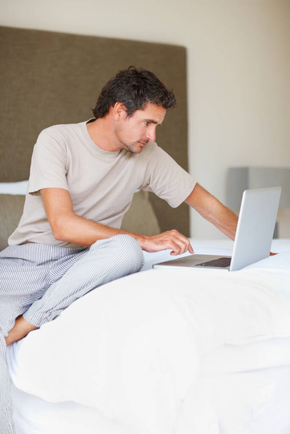 Trabajo desde casa. Casualmente vestido hombre maduro utilizando el ordenador portátil en la cama - Foto, Imagen