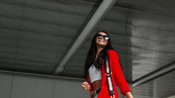 Módní krásná šťastná obchodní dívka s úsměvem v módě světlé ležérní oblečení s červeným sako, top a taška chůze a baví ve městě - Fotografie, Obrázek