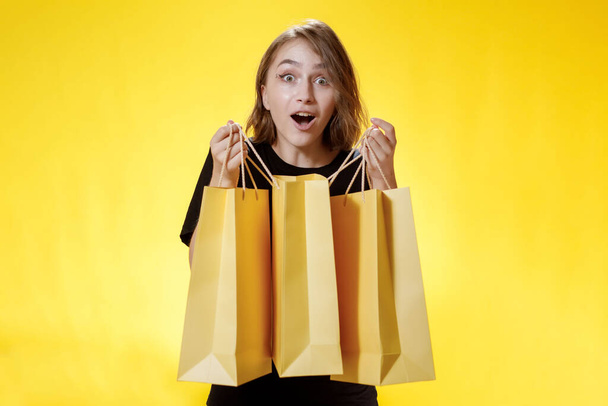 Surprised woman to big discounts with packages on yellow background, shopping trip. Studio portrait. Black friday sale. - Foto, Bild