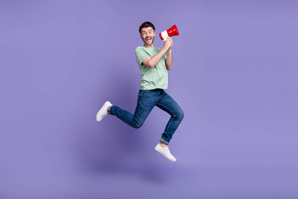 Full size photo of handsome young man jumping hold megaphone excited dressed stylish gray garment isolated on purple color background. - 写真・画像