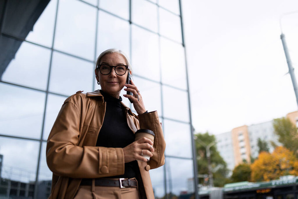femme adulte attachante parlant au téléphone avec une tasse de café dans ses mains. - Photo, image