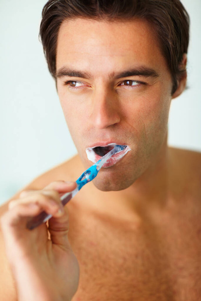 Κοντινό πλάνο ενός νεαρού προνοητικού άντρα να βουρτσίζει τα δόντια του. Κοντινό πορτραίτο ενός σκεπτόμενου νεαρού που βουρτσίζει τα δόντια του. - Φωτογραφία, εικόνα
