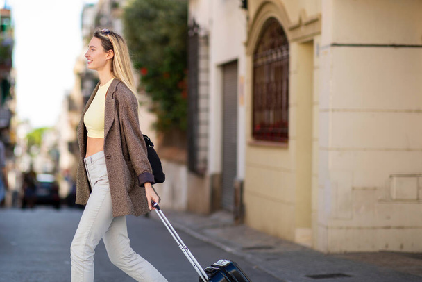 Schöne Frau zieht Reisetasche beim Überqueren der Straße - Foto, Bild