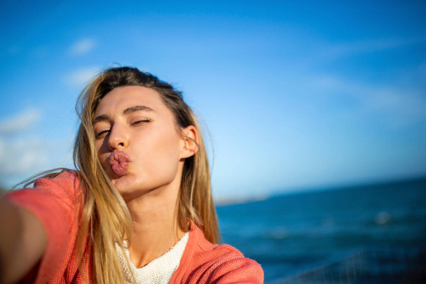 Porträt einer glücklichen jungen Frau, die ein Selfie mit einem Kuss am Meer macht - Foto, Bild