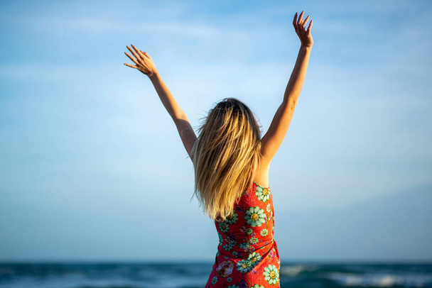 Retrato de la espalda de una joven con los brazos levantados por la orilla del mar  - Foto, Imagen