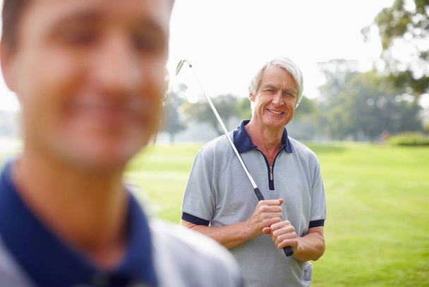 Un senior tenant un club de golf et souriant. Portrait d'un homme âgé tenant un club de golf et souriant avec son fils au premier plan - Photo, image