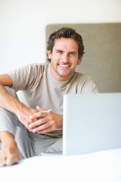Happy man using laptop in bed. Portrait of handsome man sitting with laptop on bed - Foto, Imagem