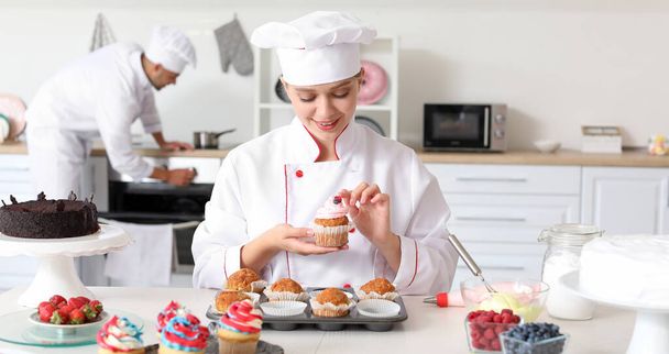 女性のお菓子はキッチンでおいしいカップケーキを飾る - 写真・画像