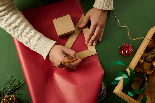 Mani femminili vista dall'alto utilizzando una matita di legno e righello triangolare disegno su una carta da imballaggio rossa, calcolando la quantità di esso per avvolgere i regali per San Valentino, Natale o Capodanno - Foto, immagini