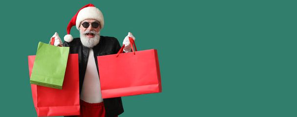 Cooler Weihnachtsmann in Lederjacke mit Einkaufstaschen auf grünem Hintergrund mit Platz für Text - Foto, Bild
