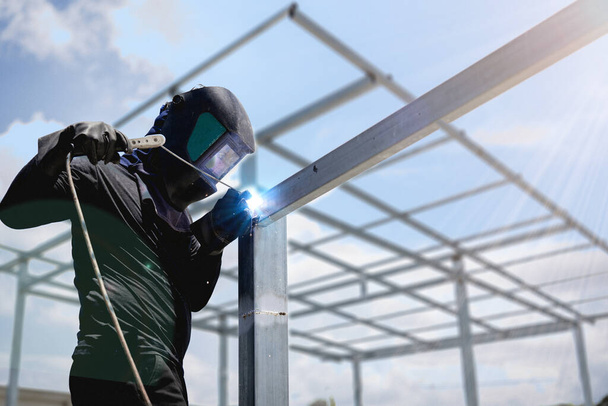 Мужчина, работающий на стальном столбе сварочной машины, синие искры от сварки, носить маску и перчатки для безопасности строительства. размытый стальной фон - Фото, изображение